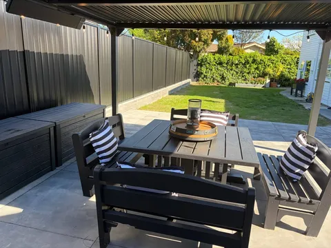 Black Colorbond fence beside a concrete patio with a pergola and outdoor dining setting, Palmerston North