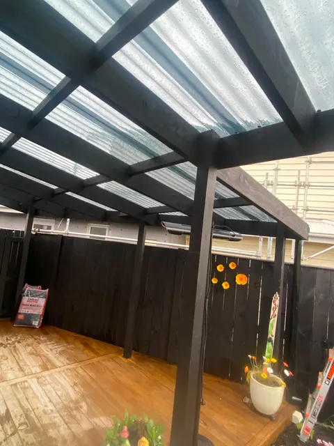 Timber deck under a dark-framed polycarbonate roof with outdoor furniture, Palmerston North